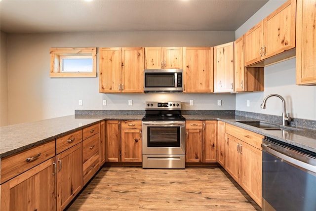 kitchen with kitchen peninsula, appliances with stainless steel finishes, dark stone countertops, light hardwood / wood-style flooring, and sink