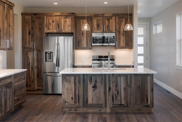 kitchen with sink, hanging light fixtures, stainless steel appliances, and a kitchen island with sink