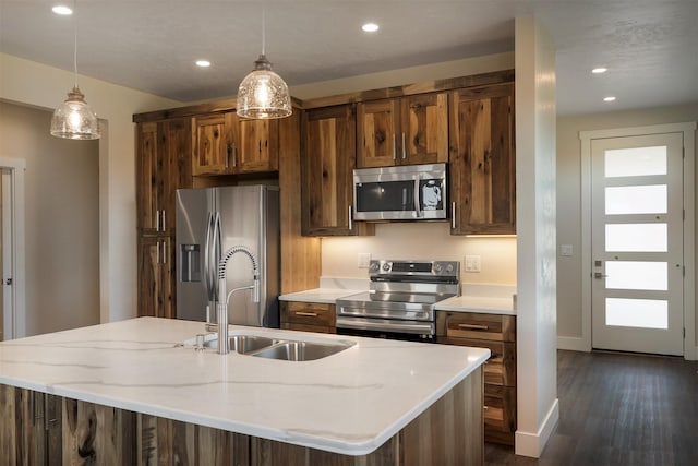 kitchen featuring appliances with stainless steel finishes, decorative light fixtures, a healthy amount of sunlight, sink, and a center island with sink