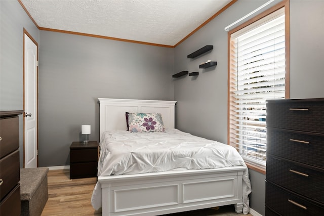 bedroom featuring a textured ceiling, ornamental molding, and light hardwood / wood-style flooring