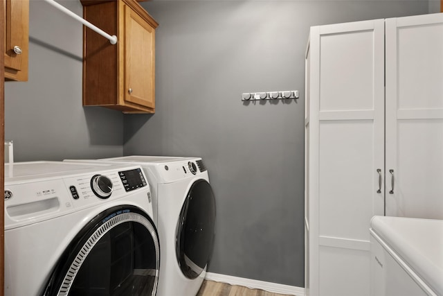 clothes washing area featuring washer and dryer, cabinets, and light hardwood / wood-style floors