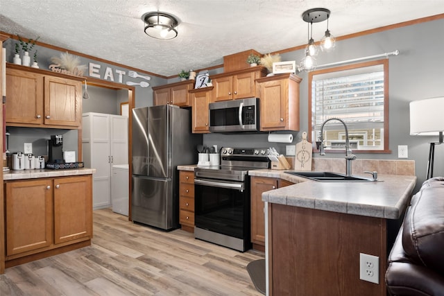 kitchen featuring stainless steel appliances, sink, hanging light fixtures, ornamental molding, and light hardwood / wood-style flooring