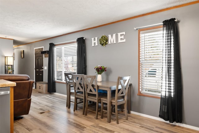 dining room with light hardwood / wood-style floors, a textured ceiling, ornamental molding, and a healthy amount of sunlight