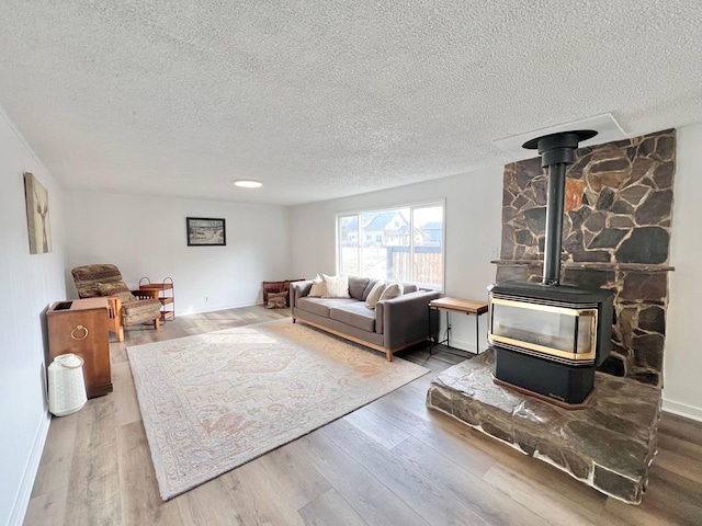 living room featuring baseboards, a textured ceiling, wood finished floors, and a wood stove