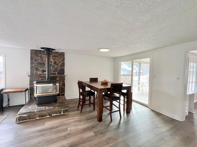 dining room with a wood stove, wood finished floors, baseboards, and a textured ceiling