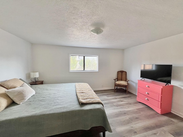 bedroom featuring a textured ceiling, baseboards, and wood finished floors