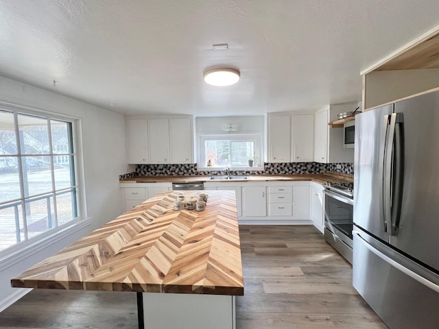 kitchen featuring light wood finished floors, decorative backsplash, appliances with stainless steel finishes, and butcher block counters