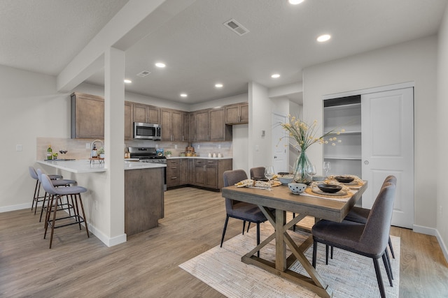 kitchen featuring kitchen peninsula, decorative backsplash, stainless steel appliances, and light hardwood / wood-style floors