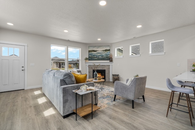 living room with a tiled fireplace, a textured ceiling, and light hardwood / wood-style floors