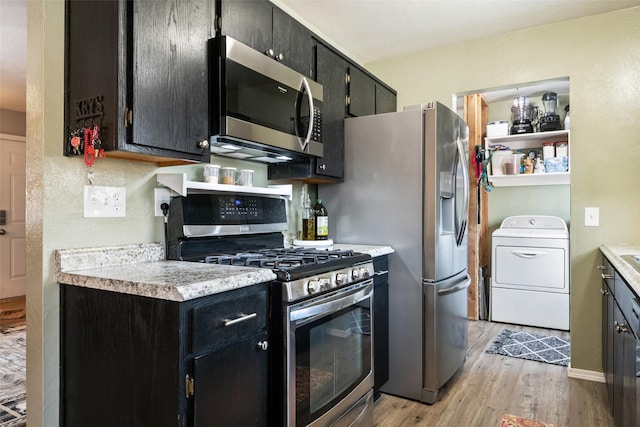 kitchen with light wood-type flooring, appliances with stainless steel finishes, and washer / dryer