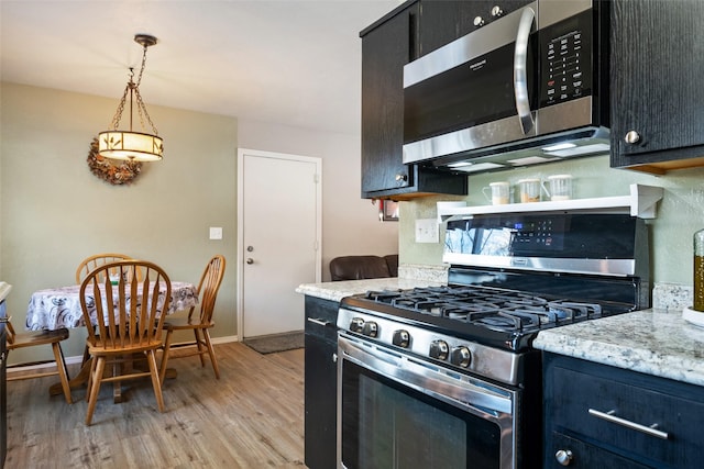 kitchen featuring light stone countertops, appliances with stainless steel finishes, light hardwood / wood-style flooring, and decorative light fixtures