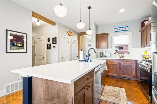 kitchen featuring pendant lighting, backsplash, a center island with sink, and stainless steel appliances