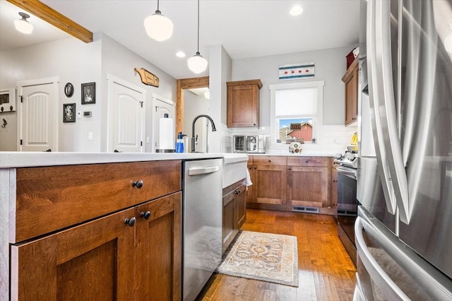 kitchen with hanging light fixtures, backsplash, stainless steel appliances, and wood-type flooring