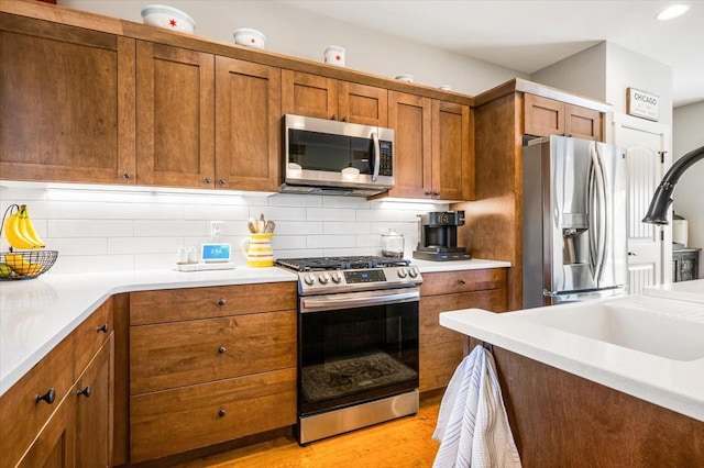 kitchen with appliances with stainless steel finishes, light hardwood / wood-style floors, and backsplash