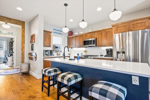 kitchen featuring decorative light fixtures, stainless steel appliances, a kitchen island with sink, a breakfast bar, and light hardwood / wood-style flooring