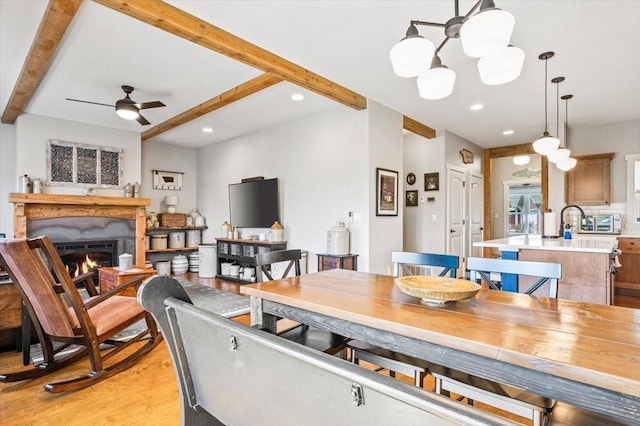 dining area featuring ceiling fan with notable chandelier, light hardwood / wood-style floors, and beam ceiling