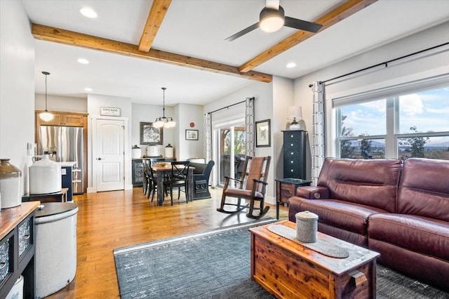 living room featuring ceiling fan with notable chandelier, light hardwood / wood-style flooring, and beamed ceiling