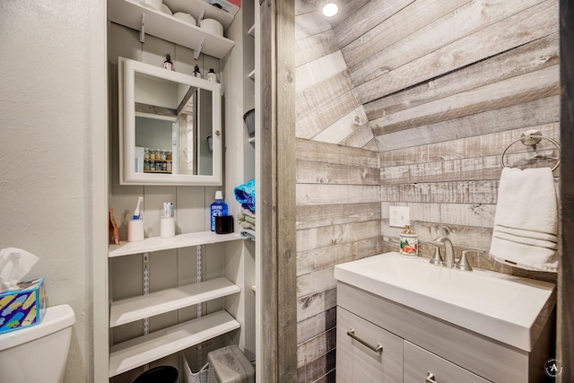 bathroom featuring toilet, wooden walls, and vanity