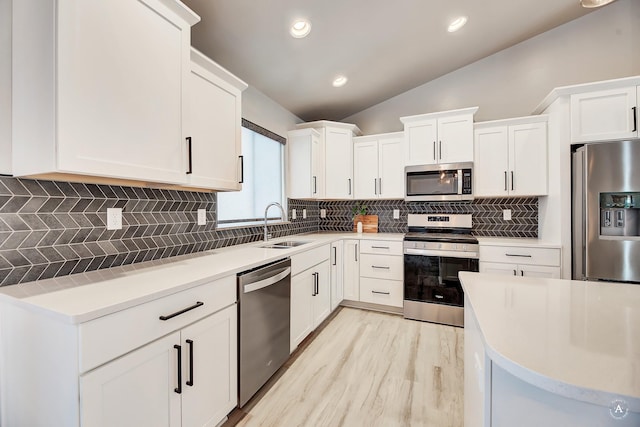 kitchen with tasteful backsplash, appliances with stainless steel finishes, vaulted ceiling, white cabinetry, and a sink