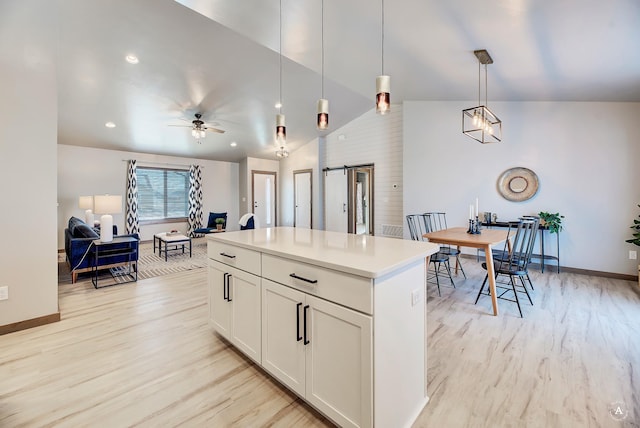 kitchen featuring a barn door, a kitchen island, a ceiling fan, light wood-style floors, and vaulted ceiling