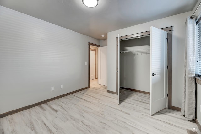 unfurnished bedroom featuring light wood-style flooring, baseboards, and a closet