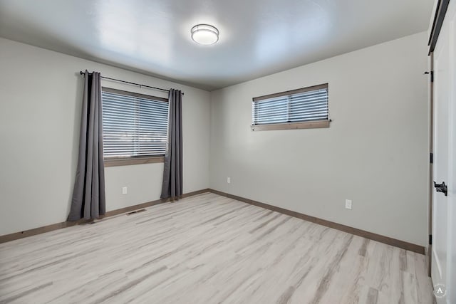 spare room featuring light wood-type flooring, baseboards, and visible vents