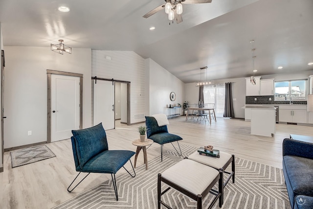 living area with lofted ceiling, light wood-style flooring, a barn door, ceiling fan, and baseboards