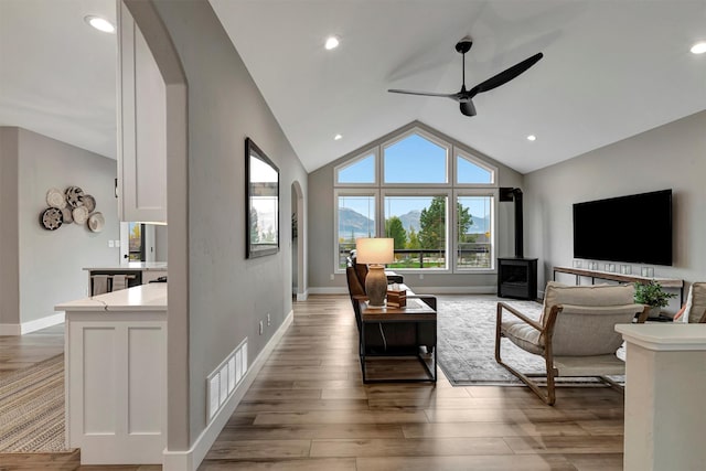 living room featuring ceiling fan, lofted ceiling, a wood stove, and light hardwood / wood-style flooring