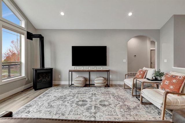 living room with light hardwood / wood-style floors, a wood stove, and vaulted ceiling