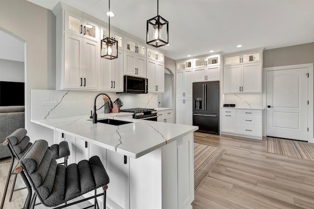 kitchen featuring a kitchen bar, backsplash, hanging light fixtures, white cabinets, and black appliances