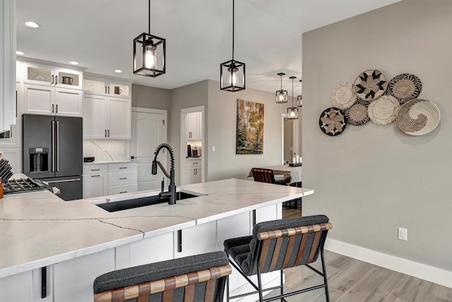 kitchen with kitchen peninsula, pendant lighting, high end black fridge, white cabinets, and sink