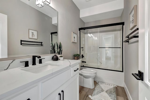 full bathroom with toilet, combined bath / shower with glass door, hardwood / wood-style floors, and vanity