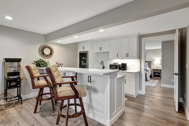 kitchen with white cabinetry, a kitchen bar, a center island with sink, light wood-type flooring, and sink