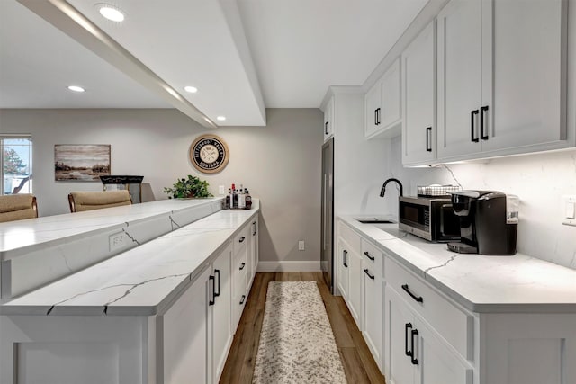 kitchen featuring white cabinetry, kitchen peninsula, wood-type flooring, light stone counters, and sink