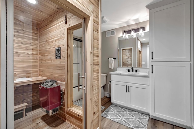 bathroom with toilet, wooden walls, wood-type flooring, and vanity