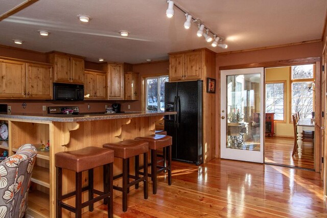 kitchen featuring track lighting, black appliances, light wood-style floors, and a breakfast bar