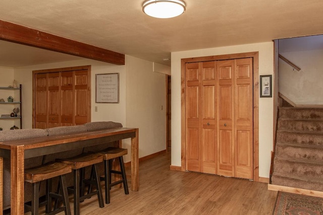 dining space with light wood-style flooring, baseboards, beam ceiling, and stairway