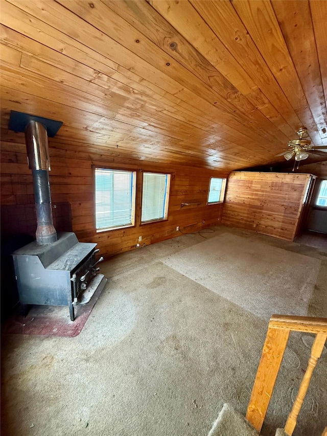 additional living space with a healthy amount of sunlight, wood ceiling, a wood stove, and ceiling fan