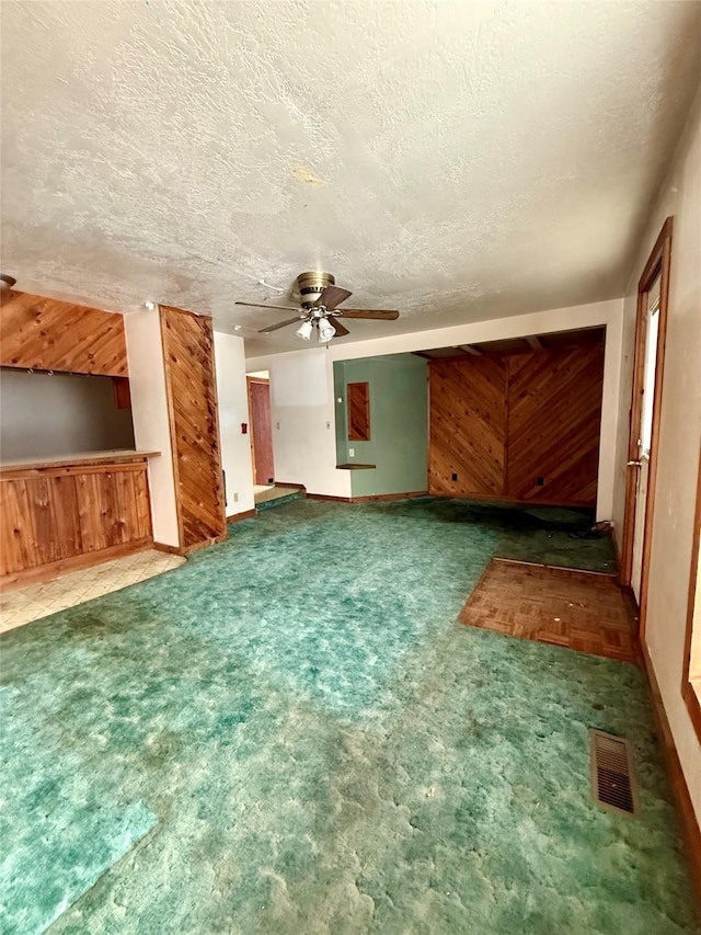 unfurnished living room with a textured ceiling, carpet floors, and wooden walls