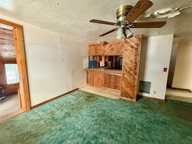 unfurnished living room featuring a textured ceiling, ceiling fan, wood walls, and carpet floors