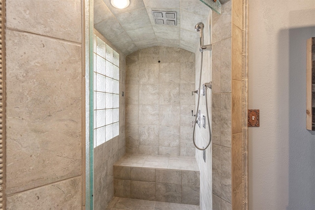 bathroom with a wealth of natural light, a tile shower, and lofted ceiling