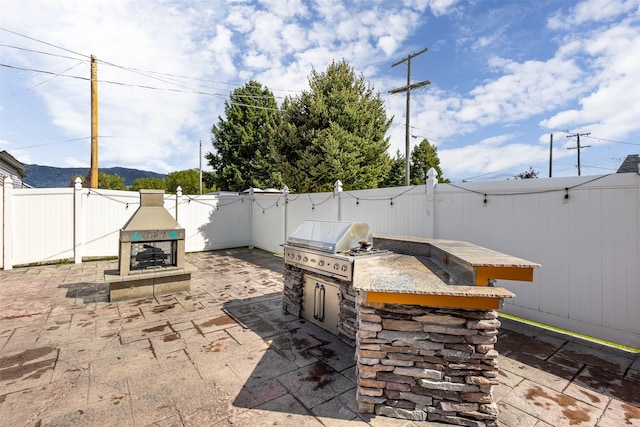 view of patio featuring exterior kitchen, an outdoor stone fireplace, and area for grilling