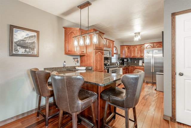 kitchen featuring pendant lighting, a breakfast bar, light wood-type flooring, appliances with stainless steel finishes, and dark stone counters