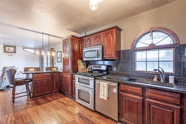 kitchen featuring pendant lighting, appliances with stainless steel finishes, tasteful backsplash, sink, and kitchen peninsula