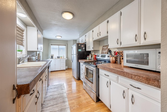 kitchen with stainless steel appliances, light hardwood / wood-style floors, white cabinetry, and sink