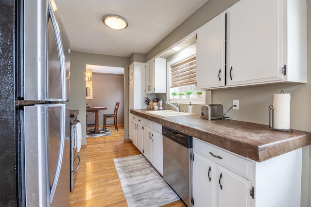 kitchen featuring white cabinets, light wood-type flooring, appliances with stainless steel finishes, and sink