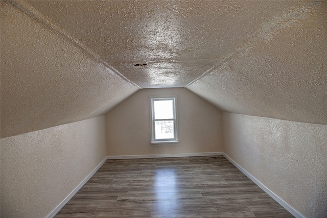 additional living space with lofted ceiling, a textured ceiling, and hardwood / wood-style flooring