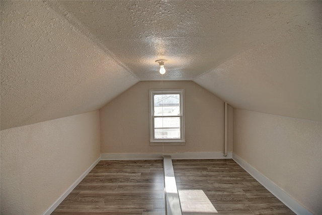 additional living space with a textured ceiling, dark hardwood / wood-style floors, and vaulted ceiling