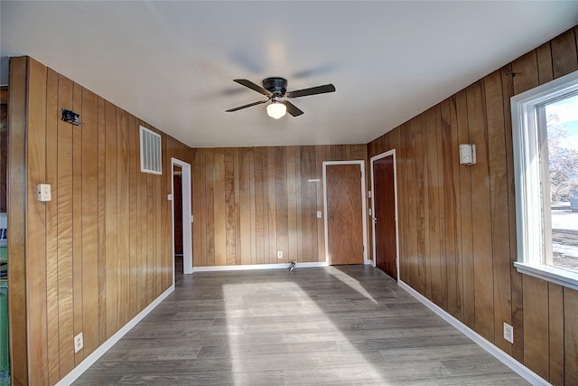 empty room with ceiling fan, light hardwood / wood-style floors, and wooden walls