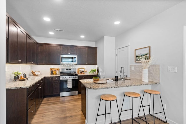 kitchen with backsplash, kitchen peninsula, sink, light wood-type flooring, and stainless steel appliances